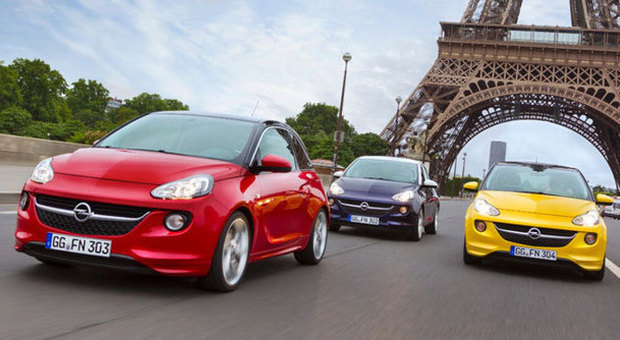 Tre Adam Opel di colori diversi tutti molto accesi, sfrercciano sotto la Torre Eiffel di Parigi