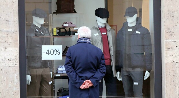 Un passante guarda la vetrina di un negozio di abbigliamento con capi in saldo