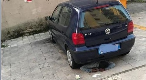 Il senzatetto dorme sotto l'auto