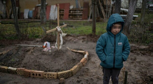 Ucraina, bambino di 6 anni accanto alla tomba della madre sepolta in giardino fa: la foto fa il giro del web