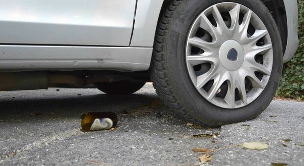 Una bottiglie di vetro spaccata sotto la gomma di una macchina in sosta