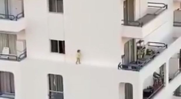 Bambina corre lungo la sporgenza di un palazzo posta al quarto piano dell'edificio