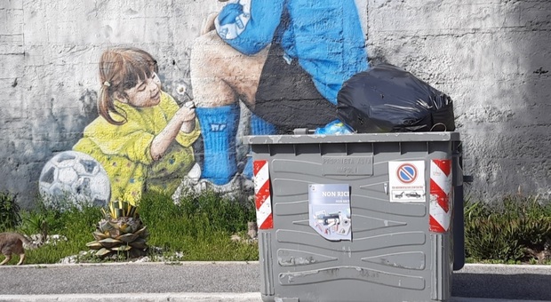 Napoli, un cassonetto davanti al murales di Maradona