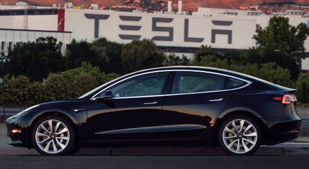 La Tesla Model 3 con alle spalle l'impianto di produzione