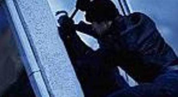 Un ladro in azione mentre forza una finestra per entrare in casa