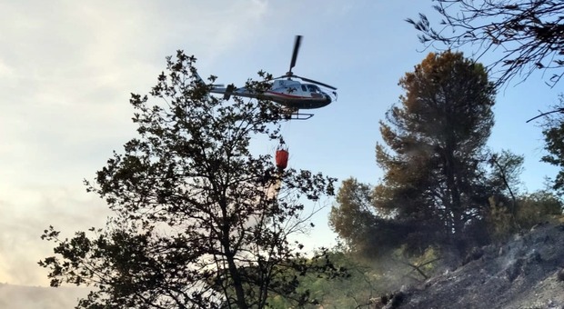 Un elicottero scarica acqua sull'incendio che imperversa nel Piceno. Caccia al piromane