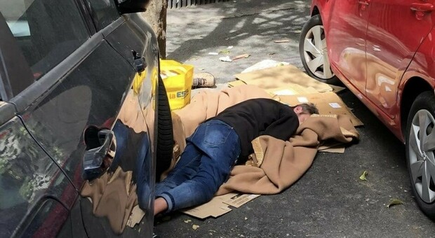 Roma, un uomo dorme avvolto nelle coperte tra le auto (e l’indifferenza dei passanti)