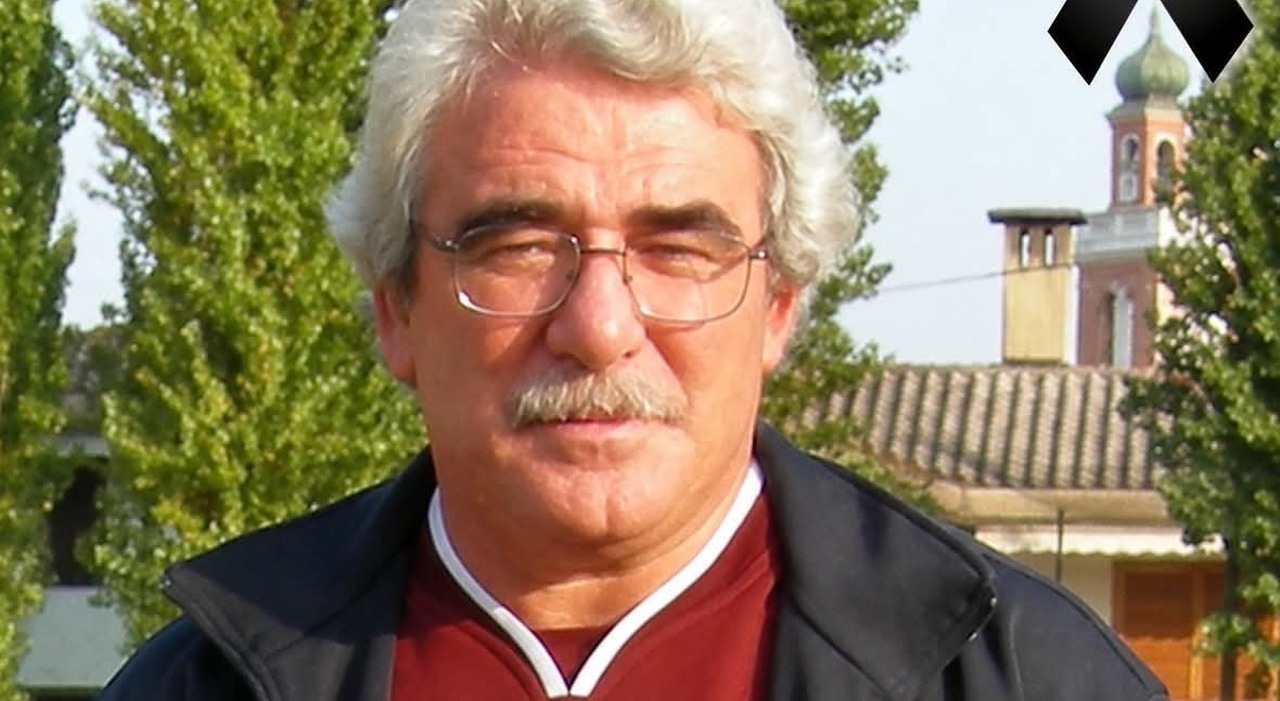 Un uomo di circa 70 anni, con un sorriso amabile, in un ambiente scolastico, circondato da studenti e amici, mentre riceve un abbraccio